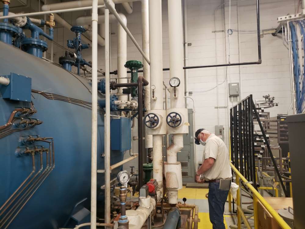 PEC employee investigating a maintenance issue with a large blue tank, valves, and piping