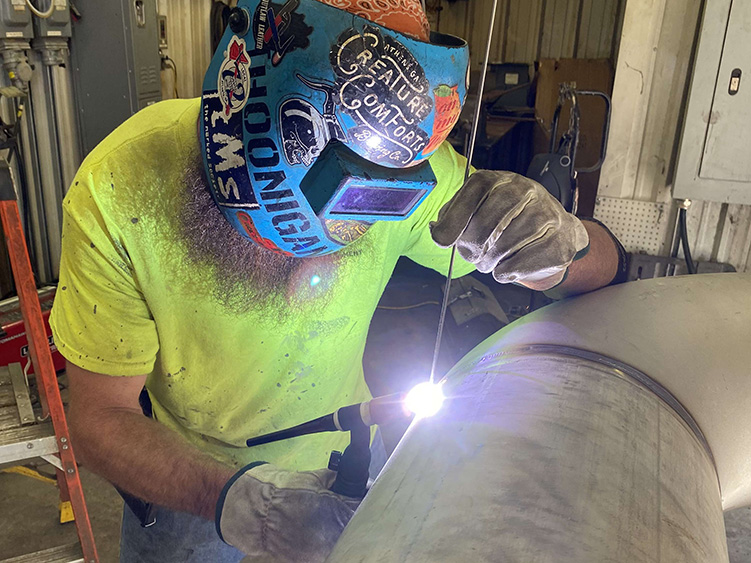 Welder in helmet welding a large metal piece in a workshop setting