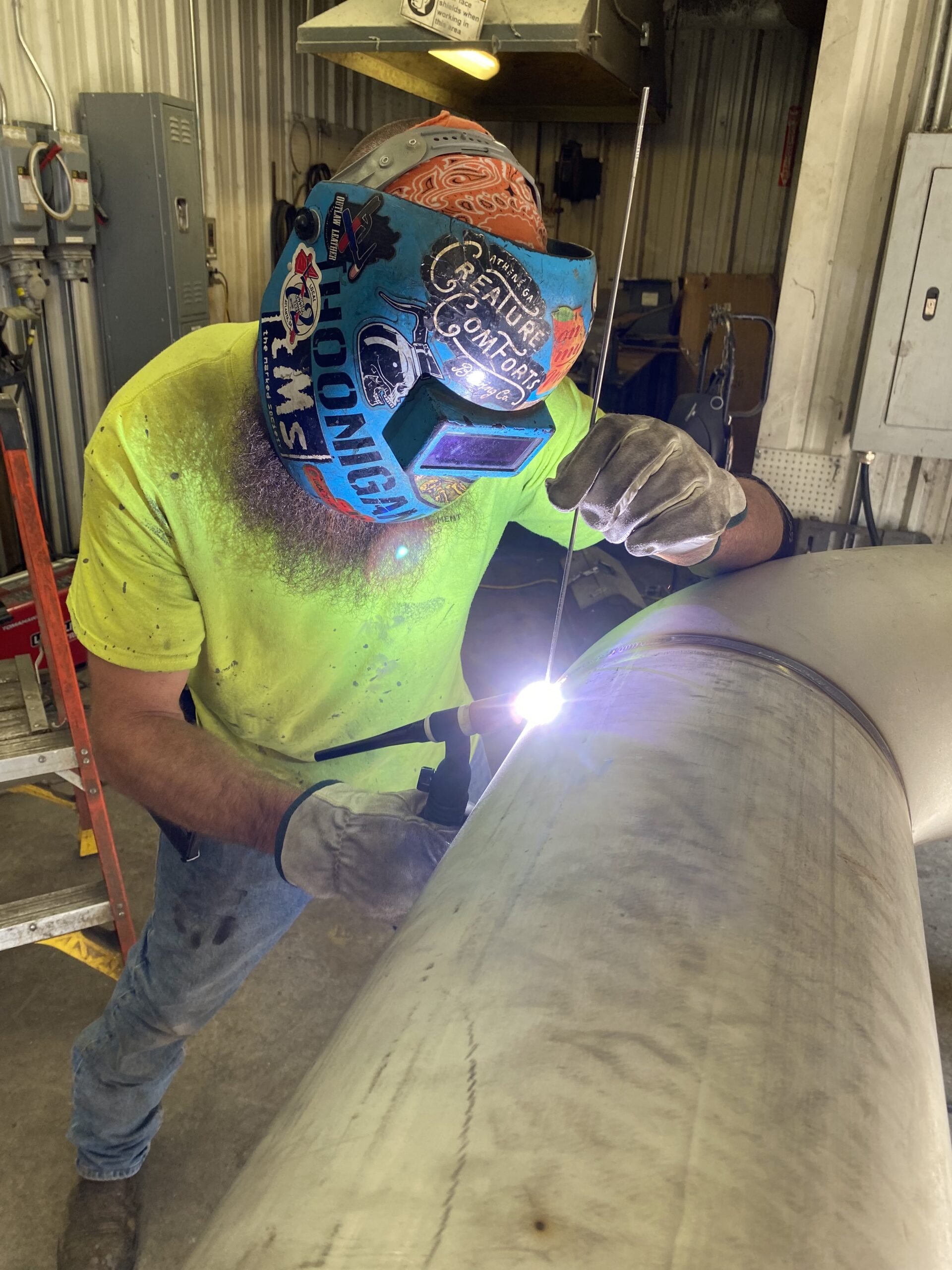 Welder in helmet welding a large metal piece in a workshop setting