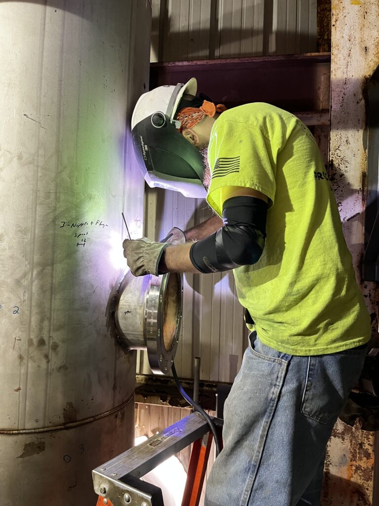 PEC welder in safety yellow shirt welding a repair in an industrial setting