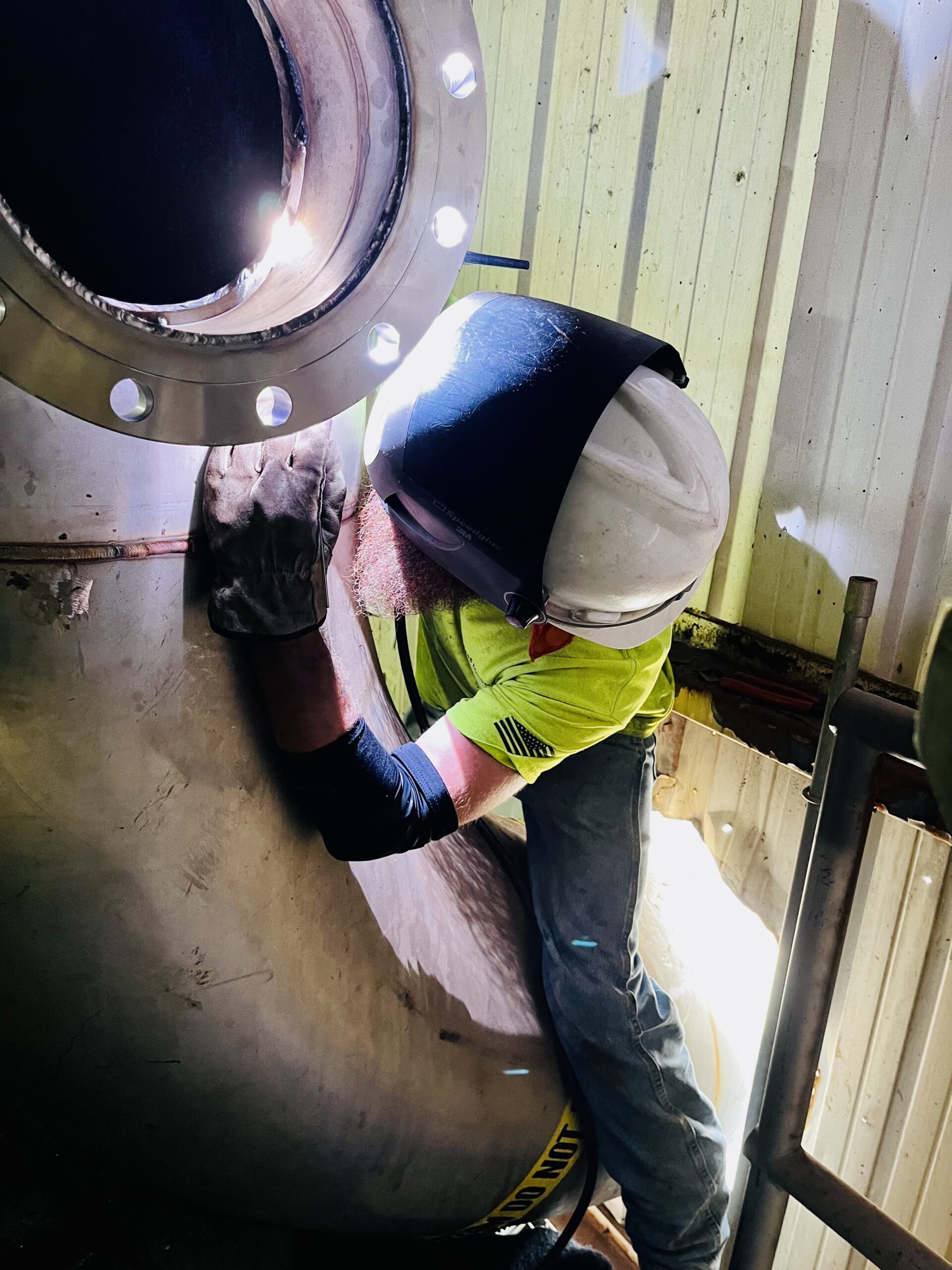 Welder in helmet working on a large metallic component.