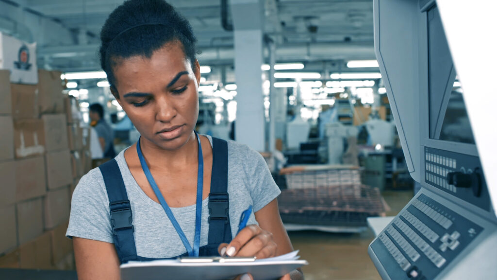 female PEC employee taking notes on clipboard surrounded by machinery and packaging