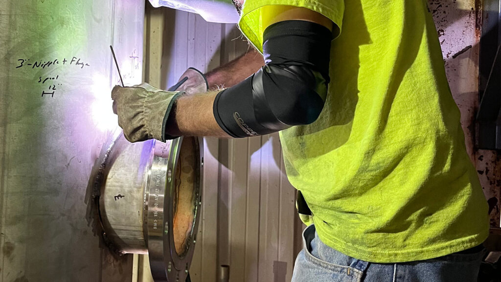 PEC welder in safety yellow shirt welding a repair in an industrial setting - landscape format